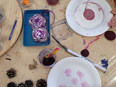 Kinder arbeiten an einem Kunstprojekt mit Wurzelgemüse, Wasserfarben und Tannenzapfen.
