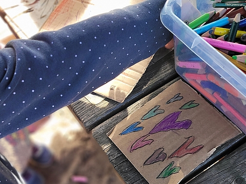 Kinder bemalen Pappen. Im Fokus ist eine mit bunten Herzen bemalte Pappe