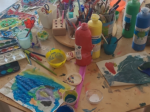 Ein Tisch voll mit Malutensilien und bunten Kunstprojekten