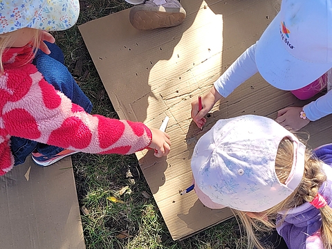 Eine Gruppe von Kindern bastelt draußen mit einem Pappkarton