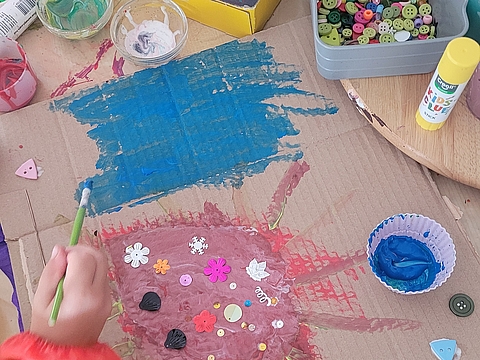 Eine Kinderhand hält einen Pinsel und malt auf einer Pappe